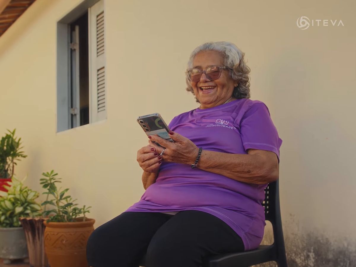 Pessoa idosa sentada numa varanda, sorrindo para o celular