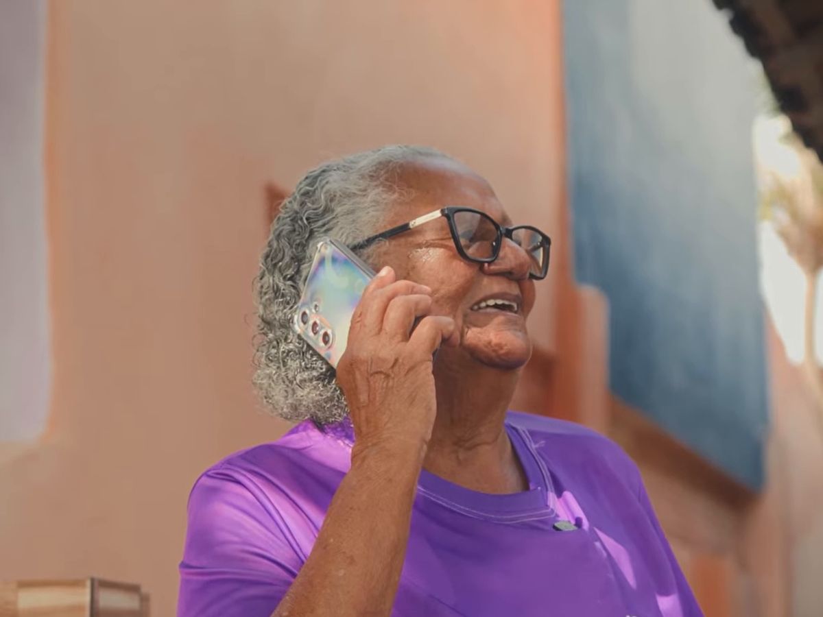Pessoa idosa de camiseta roxa sorrindo enquanto fala ao celular