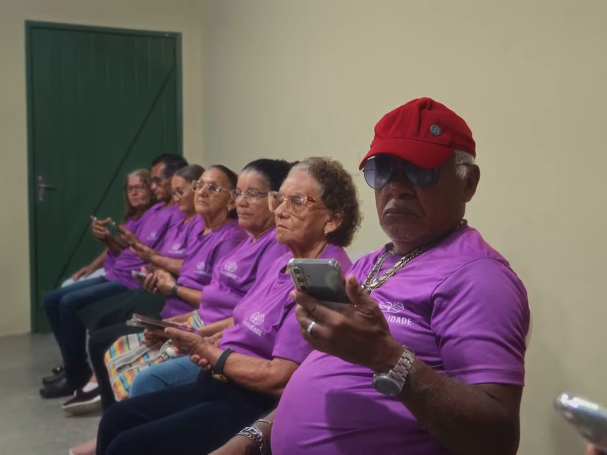 Fileira de pessoas idosas de camiseta roxa, sentadas, cada uma com o celular na mão