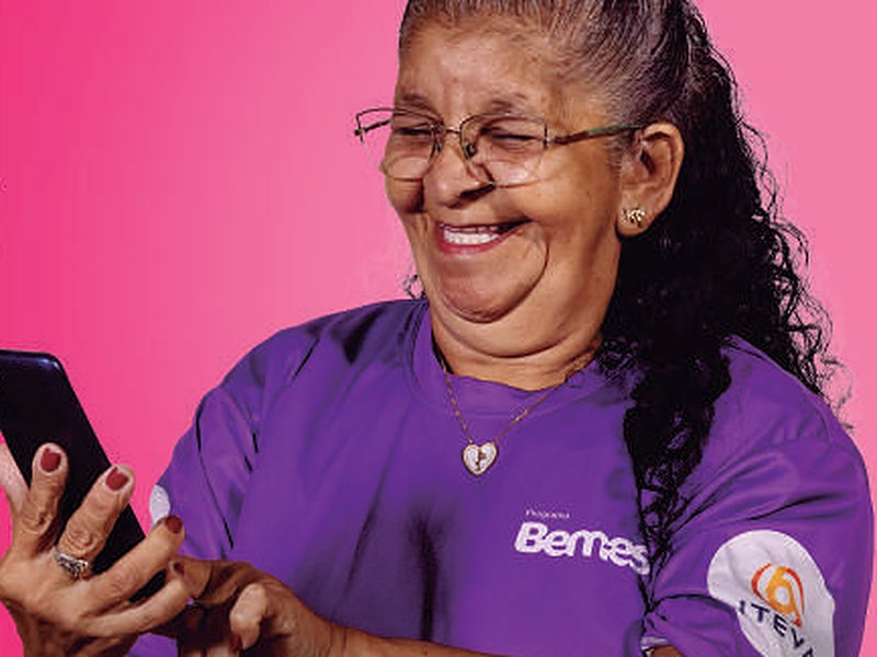 Pessoa idosa de camiseta roxa do Bem-estar +60, rindo enquanto mexe no celular